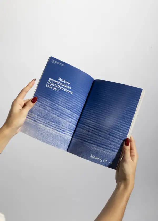 Hände mit roten Fingernägeln halten ein aufgeschlagenes Buch mit blauem Hintergrund und weißem Text