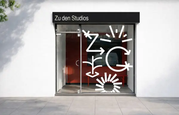 Eingangsbereich der KLOZ Studios mit weißer Fassade, Betonboden, abstrakten Grafikelementen auf der Glasscheibe und weißer Typografie „Zu den Studios“ am schwarzen Vordach.