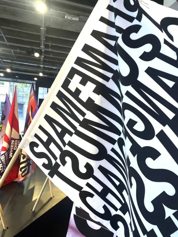 Schwarz-weiß bedruckte Fahne mit typografischen Buchstaben, aufgestellt neben weiteren gestalteten Fahnen